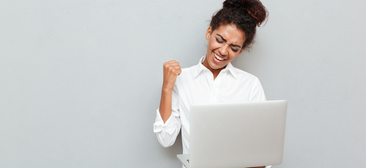 Photo of a triumphant woman with laptop in front of a grey background