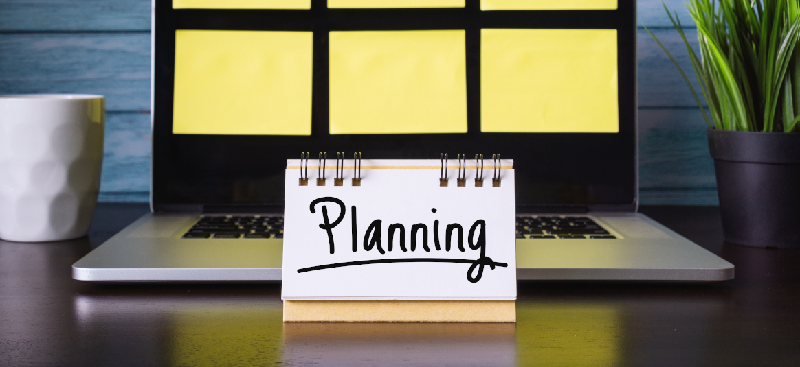 Photo of a laptop with post-it notes on screen and a sign saying “Planning”