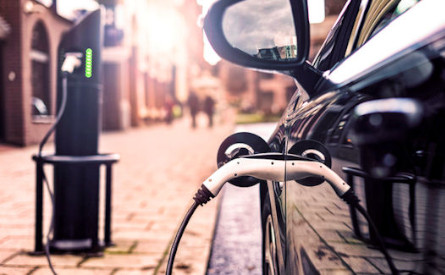 Car parked on a street and plugged into an electric charging station.